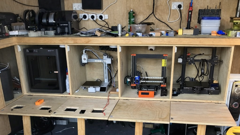 Workshop setup with multiple 3D printers on a wooden shelf.